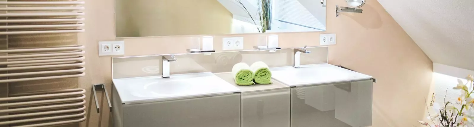 Helles modernes Badezimmer mit Doppelwaschtisch, großem Spiegel, eleganten Armaturen und Handtuchheizkörper, dekoriert mit grünen Handtüchern.