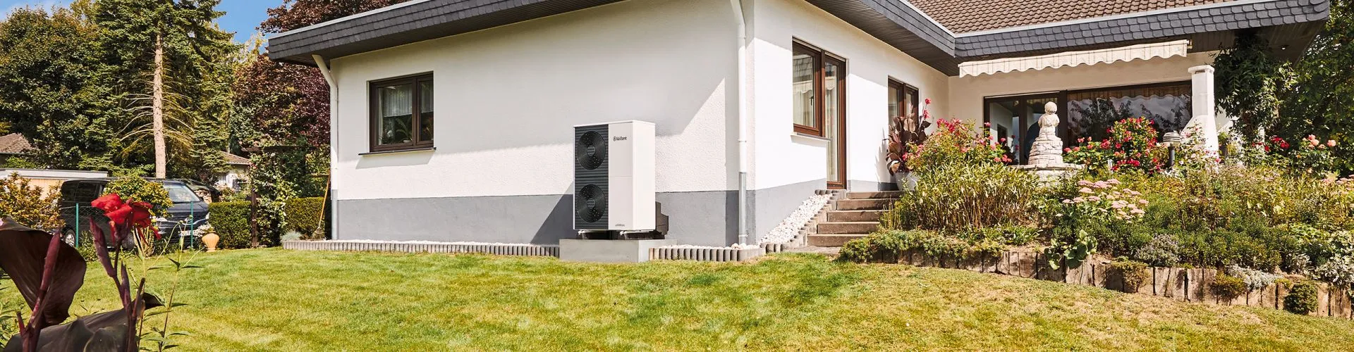 Eine Wärmepumpe von Vaillant steht vor einem Einfamilienhaus leicht erhöht auf einem Sockel.. 