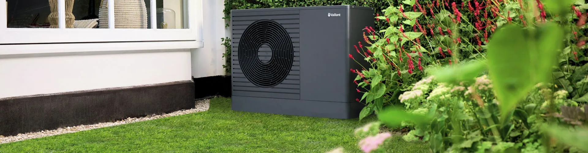 Eine moderne Vaillant-Wärmepumpe steht in einem grünen Garten vor dem Haus.