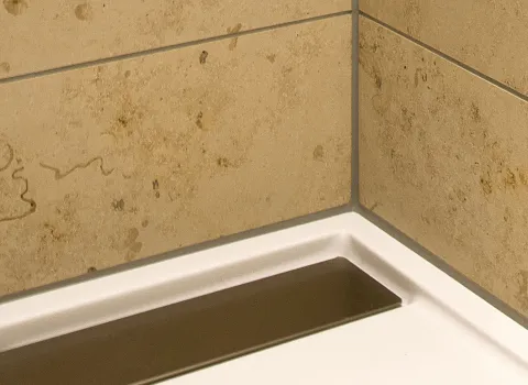 Eckbereich einer Dusche mit beigen Fliesen und sauberer Silikonversiegelung entlang der Kanten, kombiniert mit einer rechteckigen Ablaufrinne.
