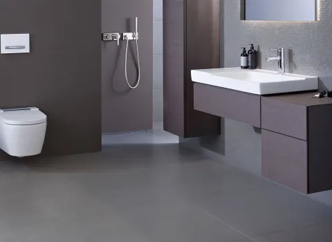 Dieses Badezimmer verfügt über ein wandhängendes Geberit AquaClean Dusch-WC, kombiniert mit einem edlen Waschtisch aus dunklem Holz und einer verchromten Wasserarmatur. 