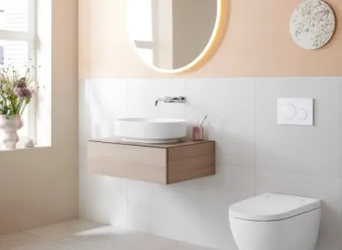 Helles Badezimmer mit dem Dusch-WC Geberit AquaClean Alba und einem schwebenden Holz-Waschtisch. Runde Spiegel und pastellfarbene Wandgestaltung.