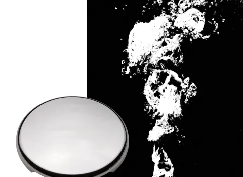 Das Bild zeigt eine Bodendüse in Chrom-Optik neben einem aufsteigenden Wasserstrom in der Whirlwanne. Die sprudelnden Bläschen verdeutlichen die Massagewirkung der Düse auf den Wannenboden.