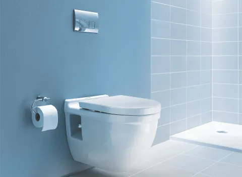 Wandhängendes Gäste-WC mit silberner Unterputzspülung im hellblau designten Badezimmer. Daneben befindet sich eine kleine Duschnische.