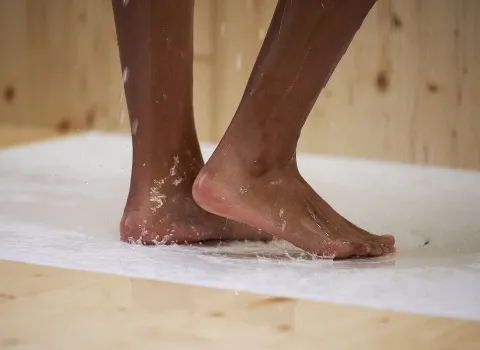 Die Füße einer Person berühren eine weiße, leicht nasse Oberfläche, auf der sich Wassertropfen sammeln.