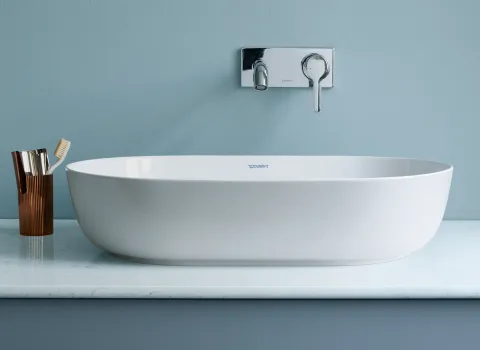 Ein modernes, ovales Waschbecken der Marke Duravit steht auf einer hellen, marmorierten Ablage vor einer blauen Wand.