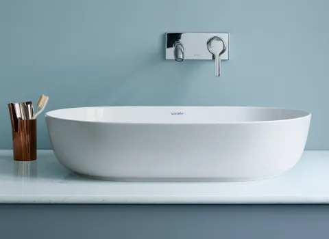 Ein modernes, ovales Waschbecken der Marke Duravit steht auf einer hellen, marmorierten Ablage vor einer blauen Wand.