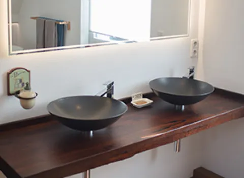 Doppelwaschplatz mit zwei schwarzen Aufsatzwaschbecken auf dunkler Holzplatte, großem Spiegel und moderner Armatur in einem hellen Badezimmer.