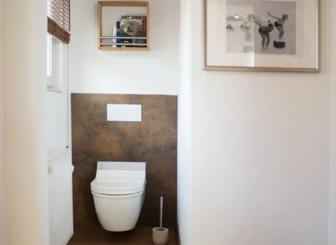 Modernes WC mit Wandnische, hängender Toilette, Holzfußboden, Wandverkleidung in Rostoptik und kleiner Wandlampe über einem Regal mit Zeitschriften.