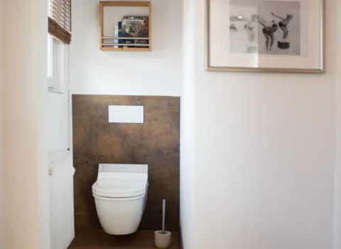 Modernes WC mit Wandnische, hängender Toilette, Holzfußboden, Wandverkleidung in Rostoptik und kleiner Wandlampe über einem Regal mit Zeitschriften.