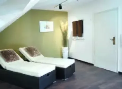 Heller Wellnessbereich mit zwei Relaxliegen unter Dachschräge, grüner Akzentwand, dunklem Boden und moderner Beleuchtung.
