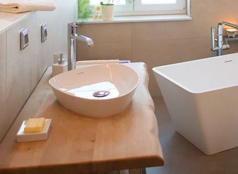 Elegantes Badezimmer mit Aufsatzwaschbecken auf einer massiven Holzplatte und moderner freistehender Badewanne vor einem Fenster mit natürlichem Licht.