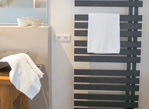 Modernes Badezimmer mit schwarzem Designheizkörper und Handtuchhalter, daneben Waschtisch mit Steinwaschbecken und Holzunterschrank.