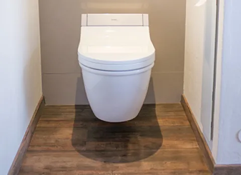 Modernes hängendes WC mit Wandverkleidung in Grau, Holzoptikboden und integrierter Bodenbeleuchtung im Badezimmer.
