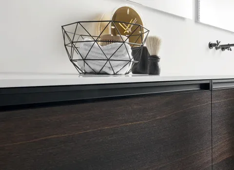 Detailansicht eines Stocco Badmöbels mit dunkler Holzfront, weißer Waschtischplatte und schwarzen Griffleisten.