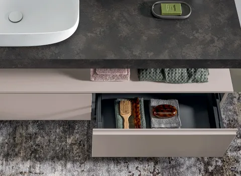 Detailaufnahme eines Stocco Badmöbels mit dunkler Steinplatte, geöffnetem Schubfach und strukturierten Handtüchern.