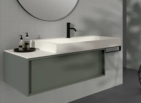 Modernes Badezimmerdesign von Stocco mit wandmontiertem Waschbecken in Weiß, grünlicher Unterschrankfront, rundem Spiegel und minimalistischer Dekoration.