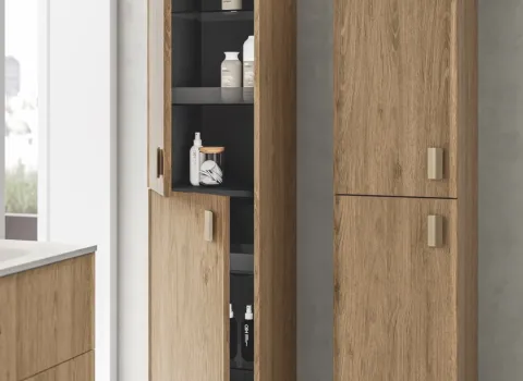 Hochschrank in warmer Holzoptik mit goldfarbenen Griffen, teilweise geöffnet mit sichtbaren Ablagefächern.