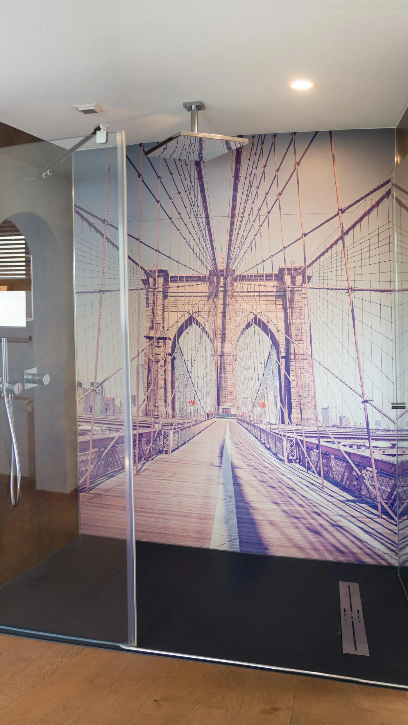 Moderne begehbare Dusche mit Glaswänden und großflächigem Fotomotiv der Brooklyn Bridge, dunkler Duschboden und Holzfußboden im Badezimmer.