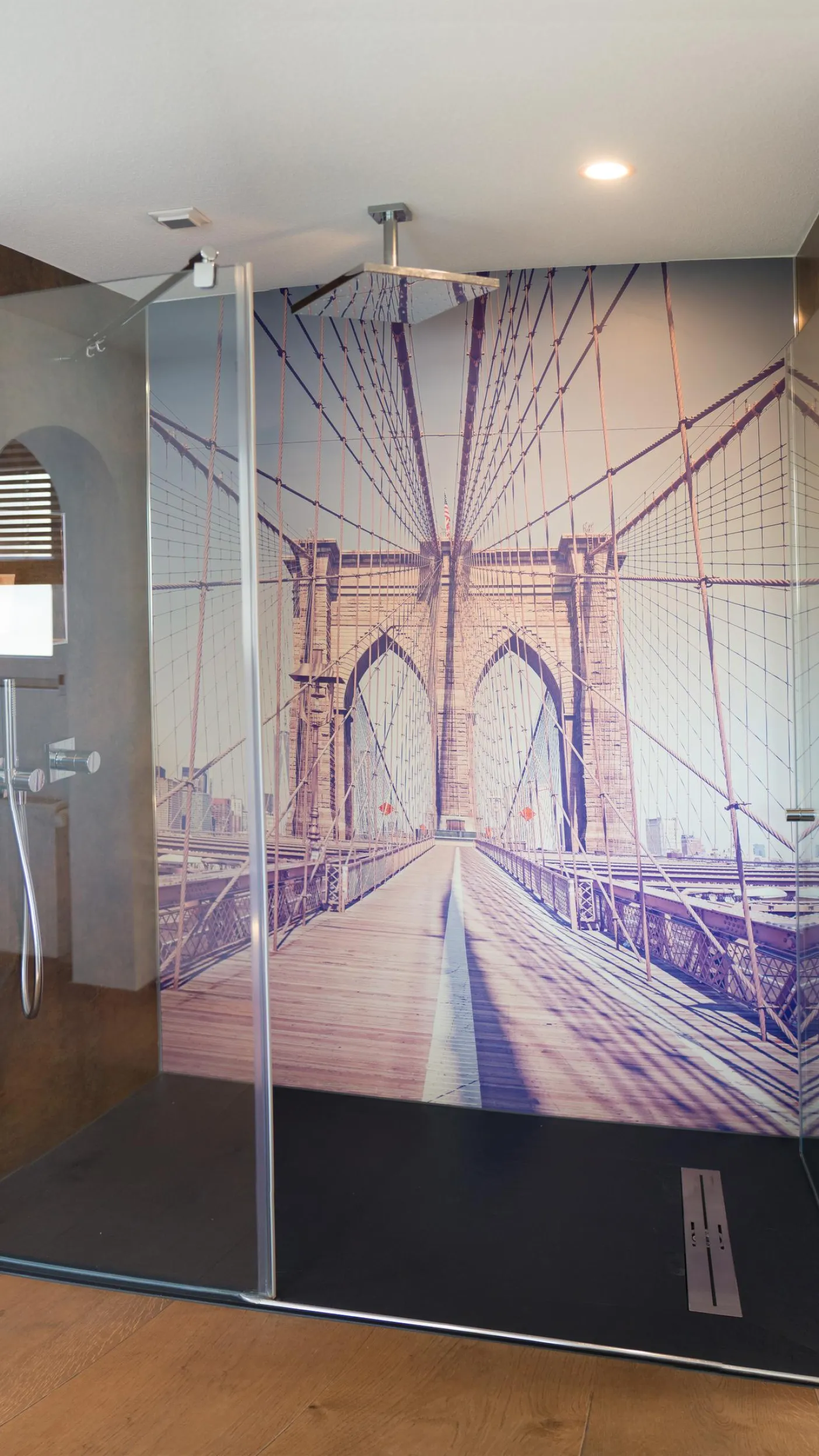 Moderne begehbare Dusche mit Glaswänden und großflächigem Fotomotiv der Brooklyn Bridge, dunkler Duschboden und Holzfußboden im Badezimmer.