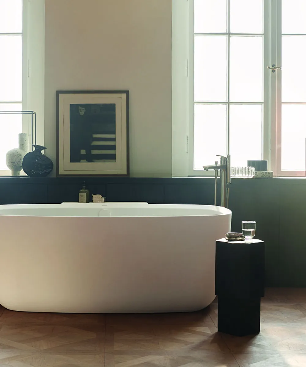 Elegantes Badezimmer mit freistehender Badewanne, großen Fenstern und stilvollen Accessoires wie Vasen und Büchern.