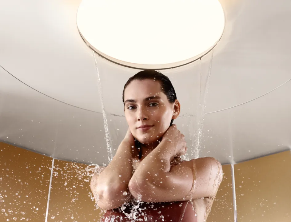 Eine Frau steht unter einer luxuriösen runden Duschbrause, während das Wasser sanft auf sie herabregnet.