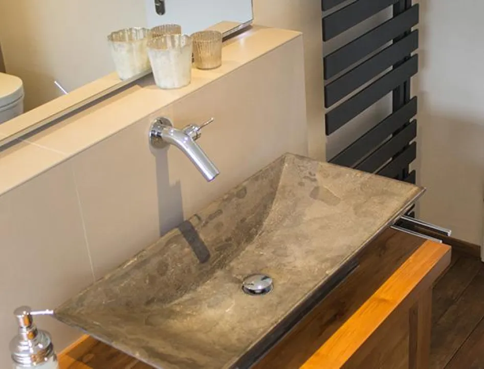 Stilvoller Waschtisch mit rechteckigem Steinwaschbecken, Wandarmatur, Holzunterbau, großem Spiegel und modernem schwarzen Handtuchheizkörper.
