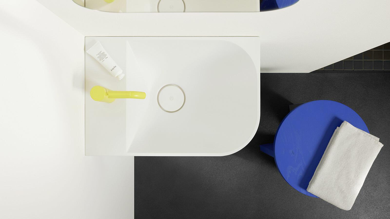 Abgerundetes Waschbecbecken und runder blauer Hocker aus Vogelperspektive